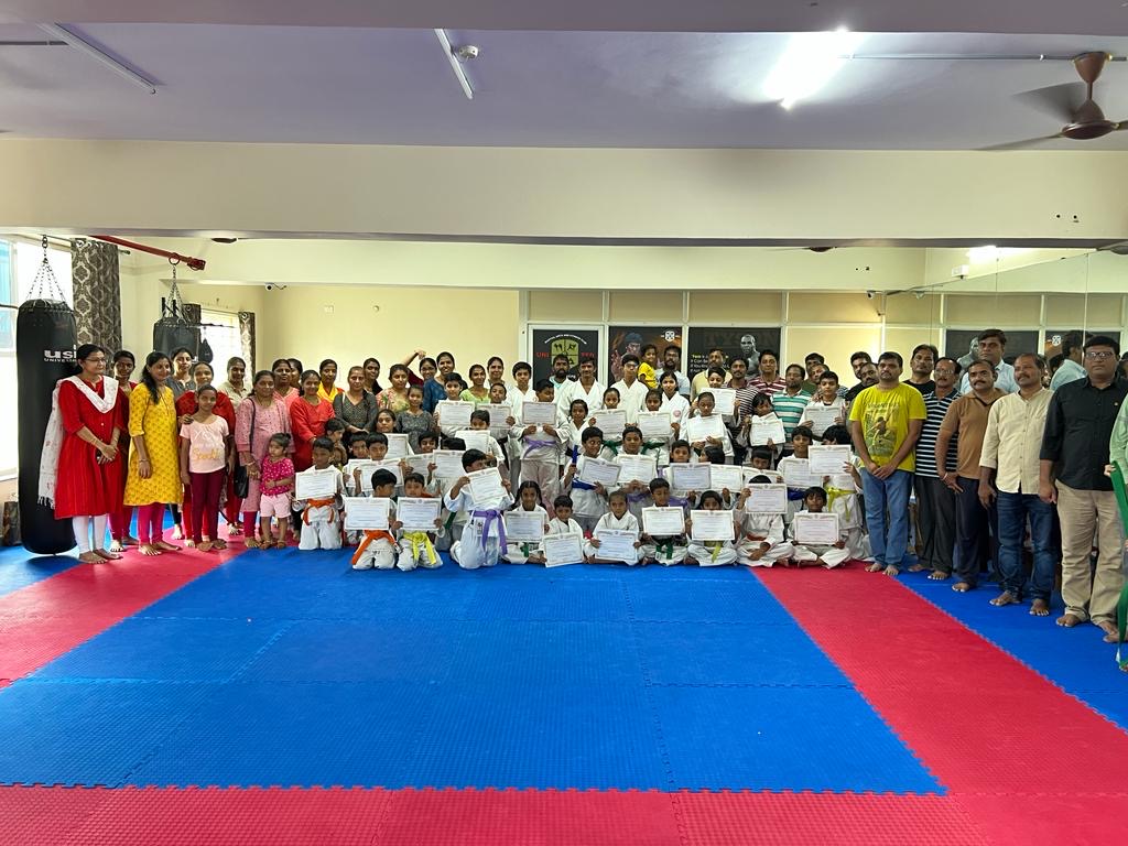 The full hall during a grading: students with certificates on the mats and parents lining the back wall.